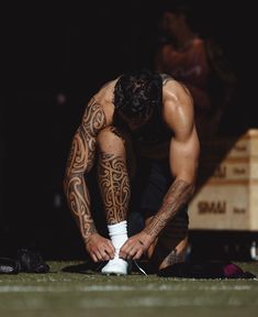 a man with tattoos on his arms and legs is tying up some white shoelaces