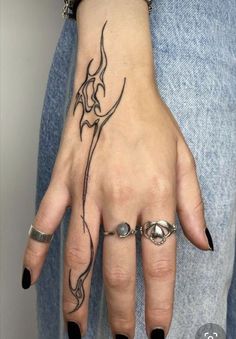 a woman's hand with tattoos and rings on her left thumb, holding onto the wrist