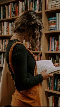 a woman standing in front of a bookshelf holding an open book