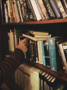 a person reaching for books on a book shelf in front of a row of books