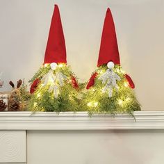 two christmas hats are sitting on top of a mantle with garland and lights around them