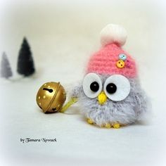 an owl with a pink hat is next to a golden bell ornament on a white surface