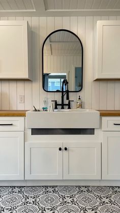 a bathroom with white cabinets and black and white tile flooring on the walls, along with a large round mirror above the sink