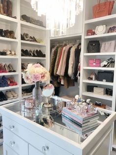 a white closet filled with lots of shoes and handbags on top of shelves next to a chandelier