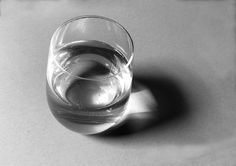 a black and white photo of a glass of water on a table top with the light reflecting off it's surface