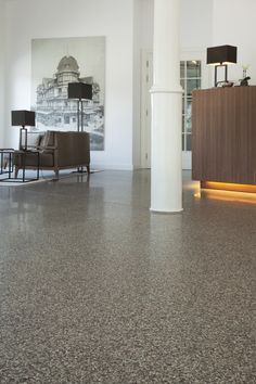 an empty lobby with two chairs and a reception desk in the center, next to a large painting on the wall