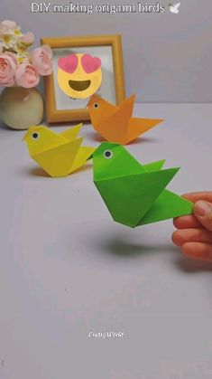 someone is holding an origami bird in front of some flowers and a picture frame