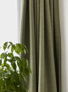 a green curtain hanging on the side of a window next to a potted plant