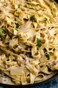 a skillet filled with pasta and meat covered in parmesan cheese, garnished with fresh herbs