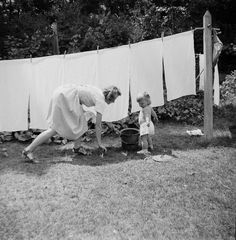 an old black and white photo of a woman hanging laundry on a clothes line next to a toddler