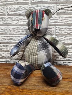 a plaid teddy bear sitting on top of a wooden floor next to a white brick wall