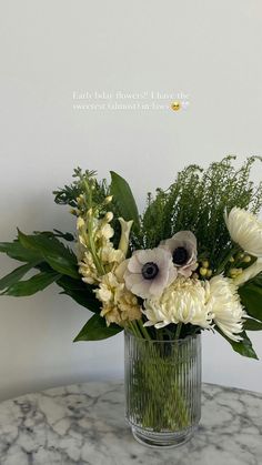 a glass vase filled with white flowers on top of a marble table next to a wall