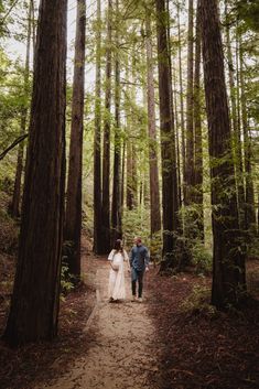 a bride and groom walking through the woods