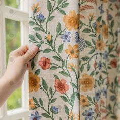 a hand is pulling up the curtains with flowers on them