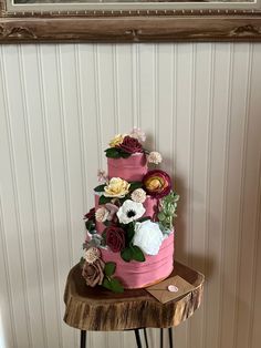 a three tiered pink cake sitting on top of a wooden table next to a painting