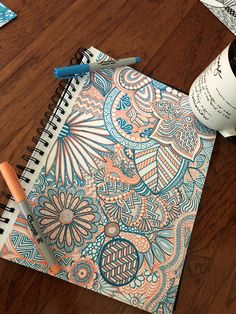 a notebook with an intricate design on it next to a cup of coffee and pen