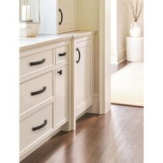 a kitchen with white cabinets and wood flooring next to a door that leads to another room