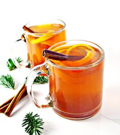 two mugs filled with orange juice and cinnamon sticks