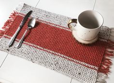 a place mat with a coffee cup, spoon and fork sitting on top of it