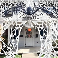 a large spider sculpture sitting in front of a white house with black and orange decorations