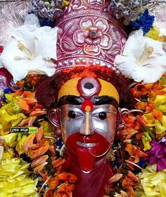 an elaborately decorated mask with flowers around it's face and head is surrounded by petals