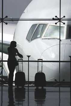 a woman standing in front of an airport gate with her luggage and looking out the window