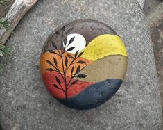 a painted rock sitting on top of a stone covered in grass and rocks with leaves