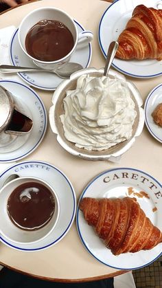 a table topped with white plates filled with desserts and pastries next to cups of coffee