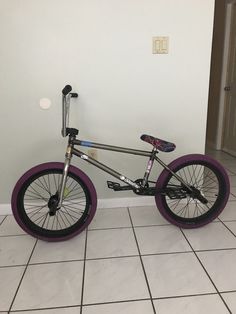 a purple and black bike sitting on top of a tile floor next to a white wall