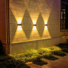 three lights that are on the side of a building in the night time, with grass growing under them