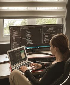 a woman sitting at a desk with a laptop in front of her and two monitors behind her