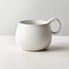 a white bowl with a curved handle sits on a countertop next to a wall