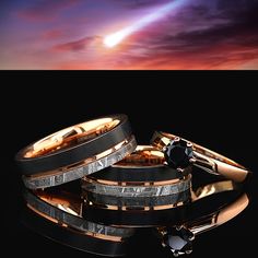 two wedding bands with black diamonds in front of a colorful sky and clouds at sunset