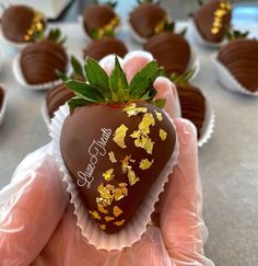 a hand holding a chocolate covered strawberry with gold flakes on it's side