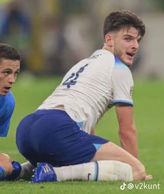 two soccer players on the field during a game, one is laying down and the other is