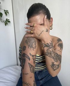 a woman with tattoos covering her face and holding her hand up to her face while sitting on a bed