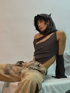 a young man sitting on top of a bed wearing a black hoodie and tan pants