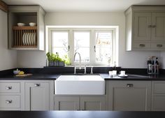 a kitchen with white cabinets and black counter tops is pictured in this image, there are two windows above the sink