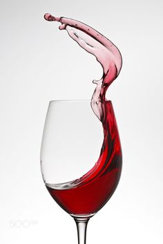 red wine being poured into a glass on a white background with water splashing from the top