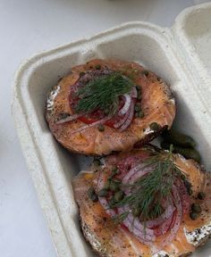 two sandwiches with salmon, onions and capers in a foam container