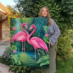 a woman standing next to a painting of two flamingos in front of some trees