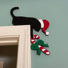 a black cat with a santa hat and candy canes hanging on the wall next to a door