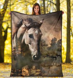 a woman holding up a large blanket with a horse on it's face and trees in the background