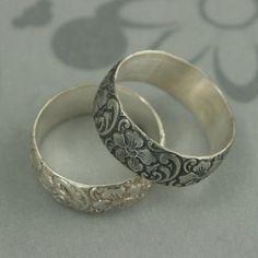 two silver wedding rings sitting next to each other on top of a gray tablecloth