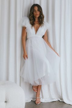 a woman standing in front of a white curtain wearing a dress with ruffles