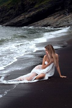 a beautiful woman sitting on top of a beach next to the ocean