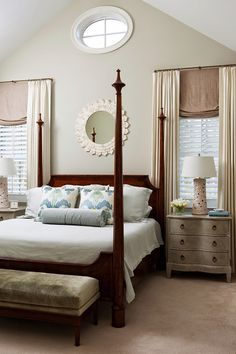 a bedroom with four poster bed, dressers and window treatments in shades of beige