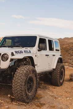 a white jeep driving on top of a dirt field next to rocks and trees in the desert