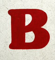 the letter b is painted red and black on concrete with white speckles around it