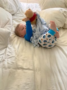 a baby laying on top of a bed with a stuffed animal